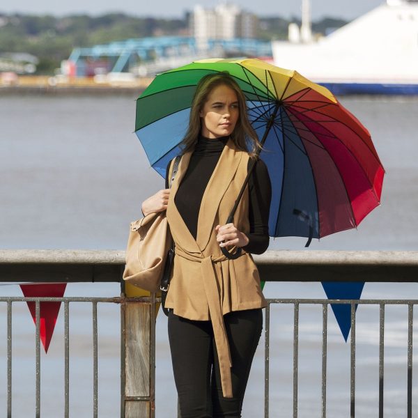 Woman holding a colourful rainbow umbrella by the river.