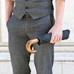 Man holding a compact black umbrella with a wooden handle.