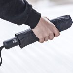Person holding a compact, automatic open and close umbrella in hand.